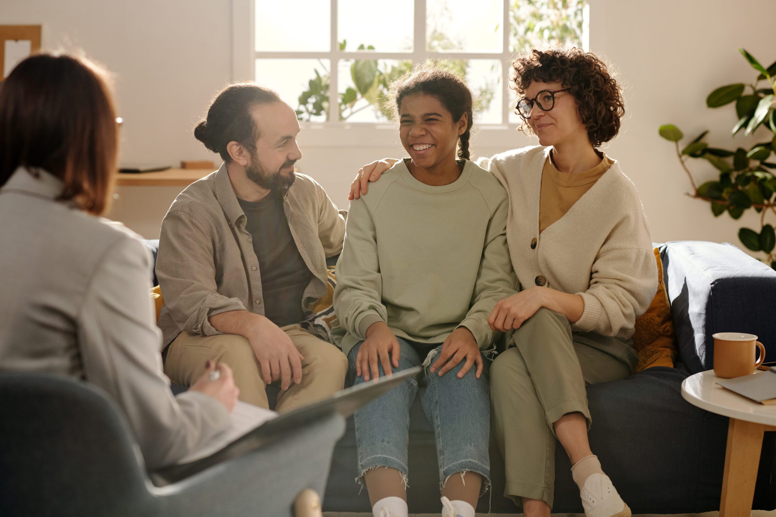 Foster parents sitting on sofa with adopted girl and talking to social worker during meeting at home